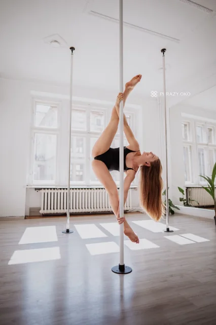 Dancer performing a pole hold with one hand on the floor